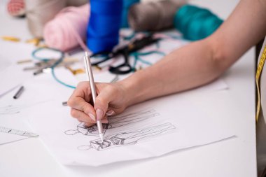 Dressmaker, moda stüdyosu kıyafet tasarımcısı masasında şık bir kalem taslağı üzerinde çalışıyor. Atölye kapanışında kıyafet süsü için dantelli unsurlar ekliyor.