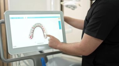Diş kliniğinde ağız boşluğu muayenesinde alternatif diş tedavi yöntemleri kullanarak bilgisayar ekranında çene modellerini gösteren siyah üniforma uzmanı