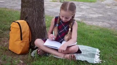 Üniformalı pozitif küçük kız ödevini yapıyor bahçedeki ağaçta oturuyor tatlı liseli kız, ilkokul derslerinden sonra parkta dinlenirken kitap yazıyor.