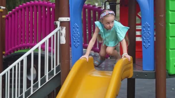 カジュアルなブルーの服の遊び心のある少女は 子供の遊び場に迷路でスライドスライド 笑顔の女子生徒は 公共の公園の子供が週末を楽しんでいるアトラクションを果たしています — ストック動画