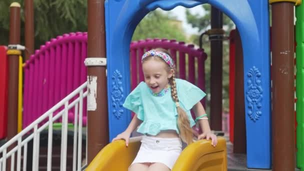 笑着的小女孩在迷宫里骑着塑料滑行在安全的儿童游乐场里快乐的孩子带着辫子在公共城市公园里玩耍 小女孩喜欢滑行 — 图库视频影像