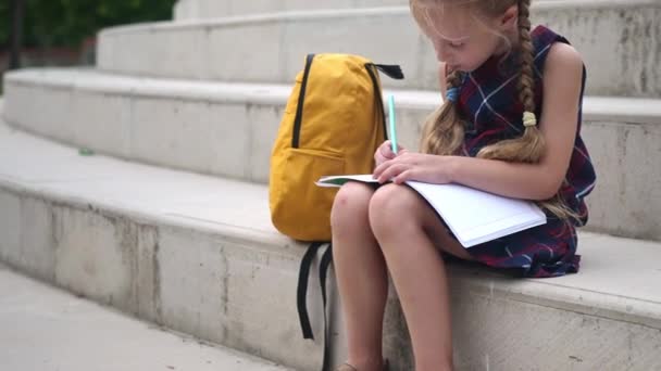 Liebenswertes Kleines Mädchen Zeichnet Schulheft Sitzt Rucksack Auf Steintreppe Blonde — Stockvideo