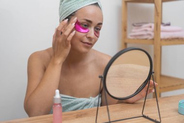 Cilt bakımı: Bir bayan, aynada, rutinini profesyonel kozmetiklerle yükseltir, pembe göz altı bantları uygular. 