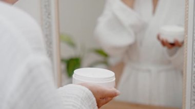 Güzellik rutini: banyoda, bir kadının elleri yaşlanma önleyici losyonu kavanozdan çıkartıp cilt bakımını arttırır.. 