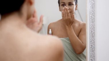 Aynanın yanında bir kadın yaşlanma önleyici cilt bakımı için serum damlası kullanarak hyalürik asit uyguluyor.. 