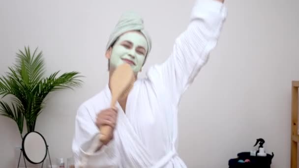 バスローブカラオケ 楽しい女性 彼女の顔に粘土マスク ヘアブラシマイクに歌い 彼女の頭の上にタオルで自宅で踊る 爆発を持って — ストック動画