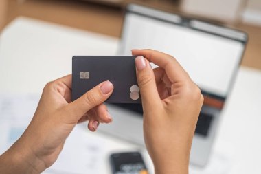 Kadın eller, evdeki belgelerle birlikte internet ödemeleri için karanlık kredi kartını masasında tutuyor. Kadın, bulanık dizüstü bilgisayarla banka sisteminde ödeme yapmayı planlıyor.