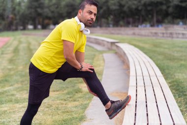 Şehir parkında esnekliğini gösteren sarı tişörtlü bir adam egzersiz yapıyor ve bacak kaslarını çalıştırıyor.. 