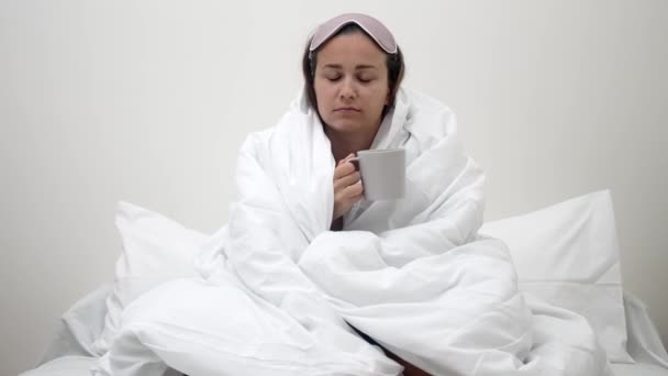 一个疲惫的女人 裹着毯子 躺在床上 手里拿着咖啡杯 生动地描写着失眠对她睡眠的影响 — 图库视频影像