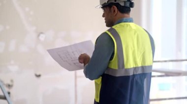 Profesyonel mimar, inşaat güvenlik ekipmanlarının yenilenmesi için çalışan üniformalı merdiven uzmanına el ele tutuşan parmak çizim kağıtlarını işaret ediyor.