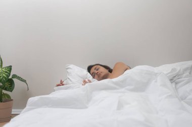 Rahatlamış bir kadın parlak bir önerme ile yatakta uyur. Esrarlı bir çiçeğin yanında. Dişi, modern bir dairede dinlenerek uykusundan enerji alır.