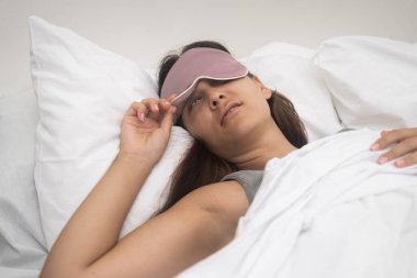 Hoşnutsuz bayan, uyku maskesi yamuk, istemeyerek ayağa kalkıyor, alarmlar açık. Uyku yoksunluğu yakın plan.. 