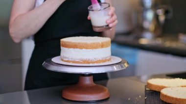 Profesyonel pastacı, pasta katmanlarını cam kavanoza krema sürmek için pembe fırça kullanıyor. Siyah önlüklü kadın. Yıldönümü kutlaması için masada duruyor.
