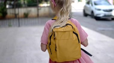 Sarı sırt çantalı küçük bir kız şehrin arka sokaklarında yürüyor. Büyük okul çantalı tatlı bir kız. Şehir çocuğu olarak okula gidiyor.