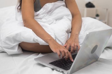 Dizüstü bilgisayarına odaklanmış bir kadın elleri, evdeki yatağının rahatlığından çevrimiçi sosyal ağlarda iletişim kuruyor.. 