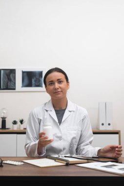 İnternette bir hastaya danışmanlık yaparken, kadın bir doktor bir şişe hap veya vitamin sunuyor, tedavi seçeneklerini tartışıyor ve reçete yazıyor. 