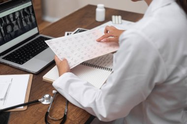 Genç bayan doktor, beyaz laboratuvar önlüklü kadının hasta muayene sonuçlarını gözden geçirir. Manyetik rezonans tomografi görüntülerine bakar.