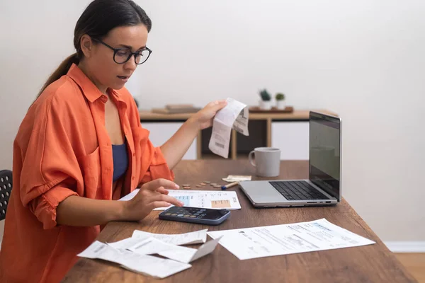 Focused female calculates utility bills with calculator on smartphone sitting at workplace with laptop woman manages budget keeping track of bank calculations accuracy