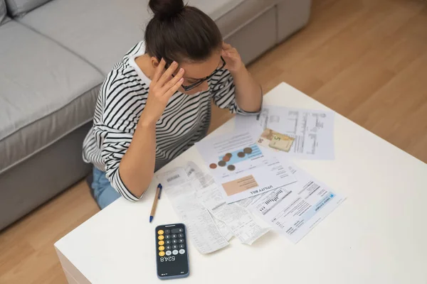 Tired lady analyses budget or utility bills counting with calculator on smartphone at home concentrated female focuses on invoice at coffee table in living room