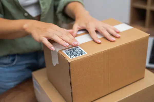 E-commerce at its core: Womans hands apply a QR code sticker to a package, symbolizing online shopping and shipping.