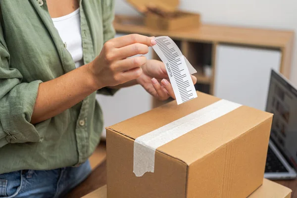 In her quest for an online shopping refund, a woman applies a barcode to a cardboard box for return.