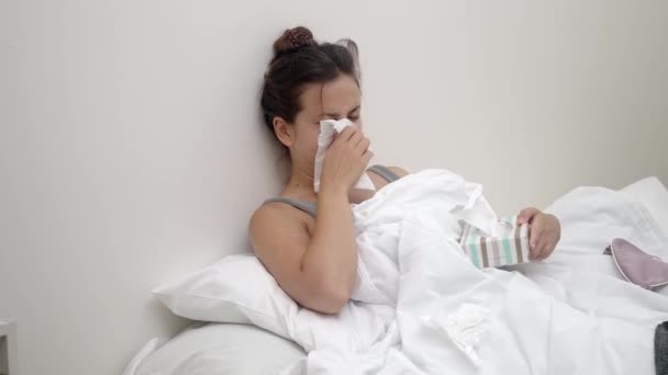 病気と戦う彼女はベッドに座り 鼻をティッシュでこぼし 医学的ドロップを保持する — ストック動画
