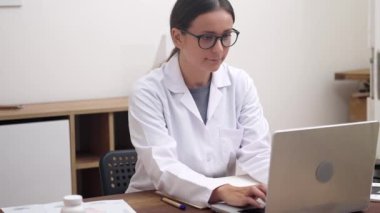 Dijital Sağlık Uzmanı: Dizüstü bilgisayarı üzerinde özenle çalışan bir kadın doktor, çevrimiçi tıbbi yardım sağlıyor, video konferansları düzenliyor ve tele sağlık kavramını somutlaştırıyor. 