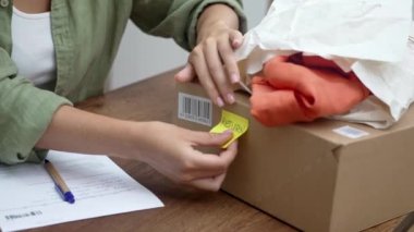 Kadın yazıyı pastalıyor. Tahta masadaki karton kutunun üzerindeki sarı etikete geri dön. Parlak şeyler paketin üzerinde çevrimiçi mağazaya dönmek için duruyor.