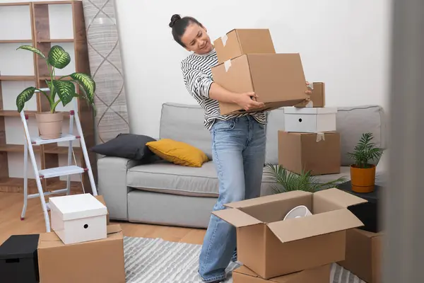 New Beginnings: A contented young woman carries a pile of cardboard moving boxes into her new apartments living room, embracing the joys of moving