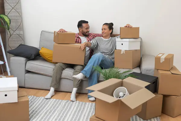 Home Sweet Home: A happy young married couple relaxes on the sofa, surrounded by numerous cardboard boxes, exhausted yet overjoyed after successfully moving to their new apartment