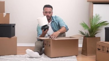 Taşınmanın ortasında, genç bir adam yeni dairesindeki paketlenmemiş kutuların arasından bir lambayı açıyor ve eve gitmeye kararlı.