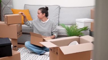 Devam edelim: Yeni evdeki genç kadın, karton kutularla çevrili, kendi dünyasını açıyor, taşınma, kiralama ya da ev sahipliğini temsil ediyor