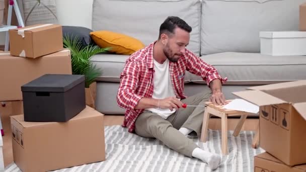 家具の芸術 カートン箱を動かす中で 若い男はDiyの棚のアセンブリで従事し 移転後の彼の新しい家に性格を注入します — ストック動画