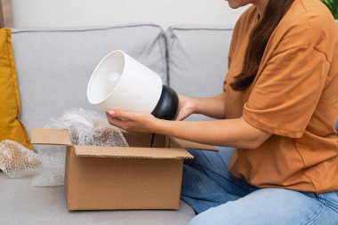 E-ticaret İçi Neşe: Sevinçle gülümseyen sanatçı, teslimat paketini teftiş ediyor, online mağazadan bulduğu ev dekorasyonunu kutluyor. 