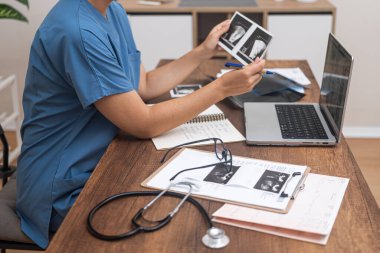 Genç bayan doktor, hasta tıp uzmanının ultrason muayenesinin fotoğraflarına bakıyor ve modern klinik bakış açısıyla bilgisayarla ve belgelerle ilgili notlar alıyor.