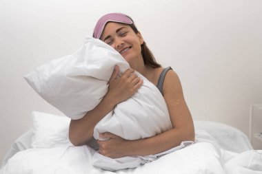 Sabah keyfi: Yatak odasında beyaz bir yastığı kucaklarken uyku maskeli güzel bir kadın ışık saçıyor.. 