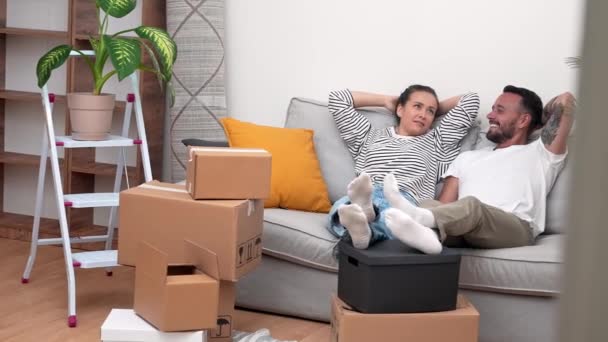 夫妻俩坐在沙发上 一边搬动着纸盒 一边心满意足地讨论着他们在新公寓里的装修和装修计划 — 图库视频影像