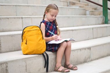 Mutlu bir liseli kız, sarı sırt çantası elinde, okuldan sonra ev ödevini özenle tamamlıyor.. 