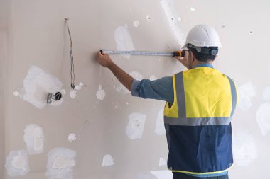 Kaliteli işçiler, eski püskü duvarın yanında dikilip şerit ile mesafeyi ölçerken koruyucu şapkalı adam ve oturma odasının içini yeniliyor.