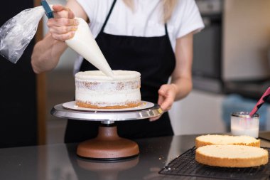 Şekersiz pasta katmanlarına beyaz krema sürerek siyah önlüklü kadınların masasında duran pastacı kadın müşteriler için lezzetli şekerlemeler yapıyor.