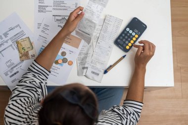 Finansal Hesaplama: Oturma odasındaki bir kadın akıllı telefon hesap makinesi ve belge kullanarak oturma odasının zeminini ve banka faturalarını hesaplıyor. 