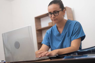 Mavi üniformalı bir doktor bilgisayarını, internet üzerinden yapılan bir muayenede hastanın test sonuçlarını titizlikle incelemek için kullanır.. 