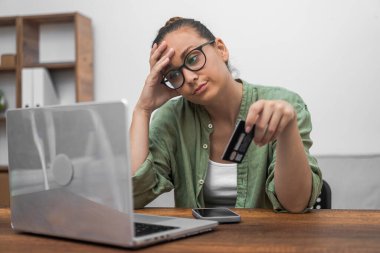 Stresli bir kadın, giderek azalan kredi kartı dengesi yüzünden üzgün bir şekilde dizüstü bilgisayarına bakıyor.. 