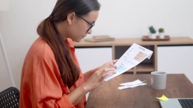 Kadın, elinde bir zarf tutarak, vergilerin ve ev giderlerinin özünü canlı bir şekilde yakalayan bir fatura üzerinde çalışıyor.