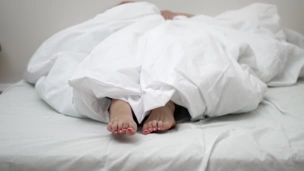 早晨的伸展 一个女人躺在床上 赤着脚从毯子里伸出手来 高兴地伸出手来迎接这一天的到来 — 图库视频影像