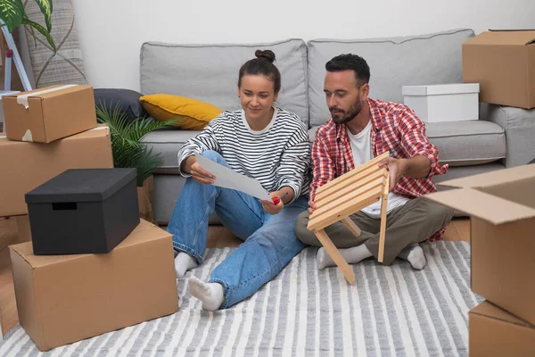 stock image Couple in love looks at instructions for assembling furniture sitting on carpet among boxes with things in cozy part of house located outside city with own plot of land