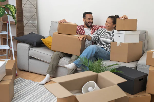 Olumlu bir çift yetişkin erkek ve kadın, oturma odasında taşınmak için paketlenmiş kutularla birlikte koltukta oturdukları için seviniyor.