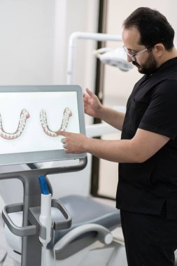 Diş kliniğinde ağız boşluğu muayenesinde alternatif diş tedavi yöntemleri kullanarak bilgisayar ekranında çene modellerini gösteren siyah üniforma uzmanı