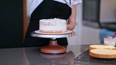 Deneyimli ev hanımı, yemek masasında duran siyah önlüklü mutfakta glüten içermeyen ürünlerden ev yapımı pasta hazırlıyor. Pişmiş tabakların etrafına beyaz krema sürüyor.