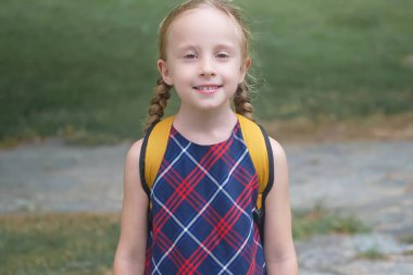 Sarı bir sırt çantasıyla sarışın liseli kız, okula giderken neşe saçıyor, okul konseptine geri dönüyor.